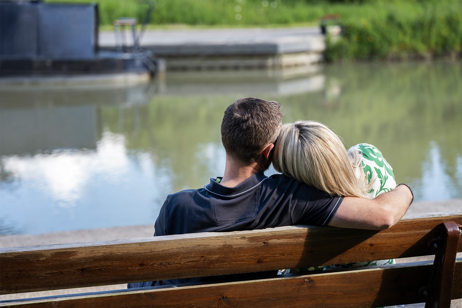 Laura og mannen sitter på en benk foran et vann med ryggen til kamera