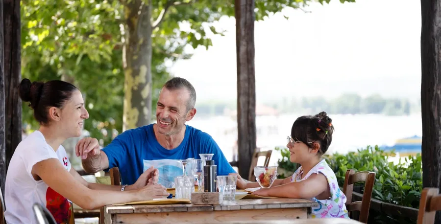 Andrea sitter ved et restaurantbord sammen med familien sin. Hvis du har spørsmål eller bekymringer om blæren og tarmen når du lever med MS, kan du kontakte Coloplast Assistanse for å få hjelp.  